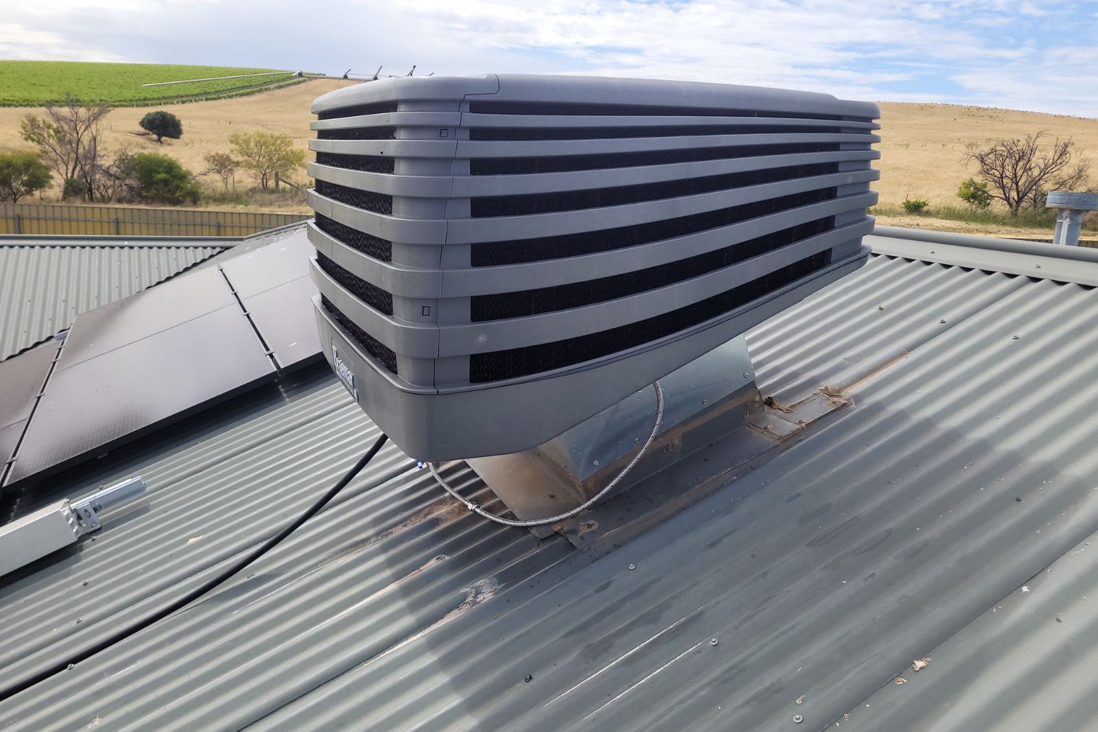 Evaporative cooling unit on roof next to solar panels